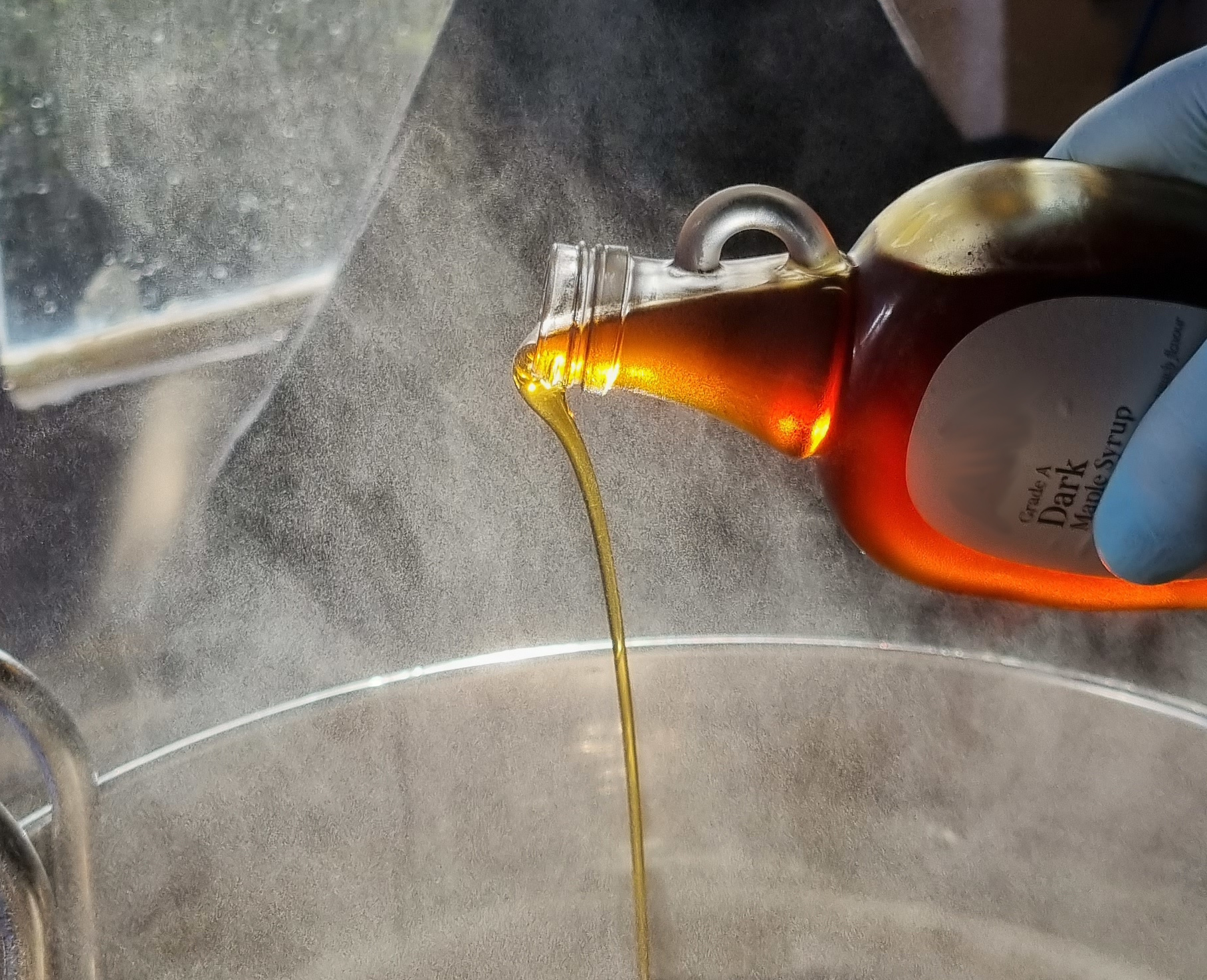 A bottle of dark maple syrup being poured into the brew kettle to trial a beer recipe for Northern Latitude's Brewery