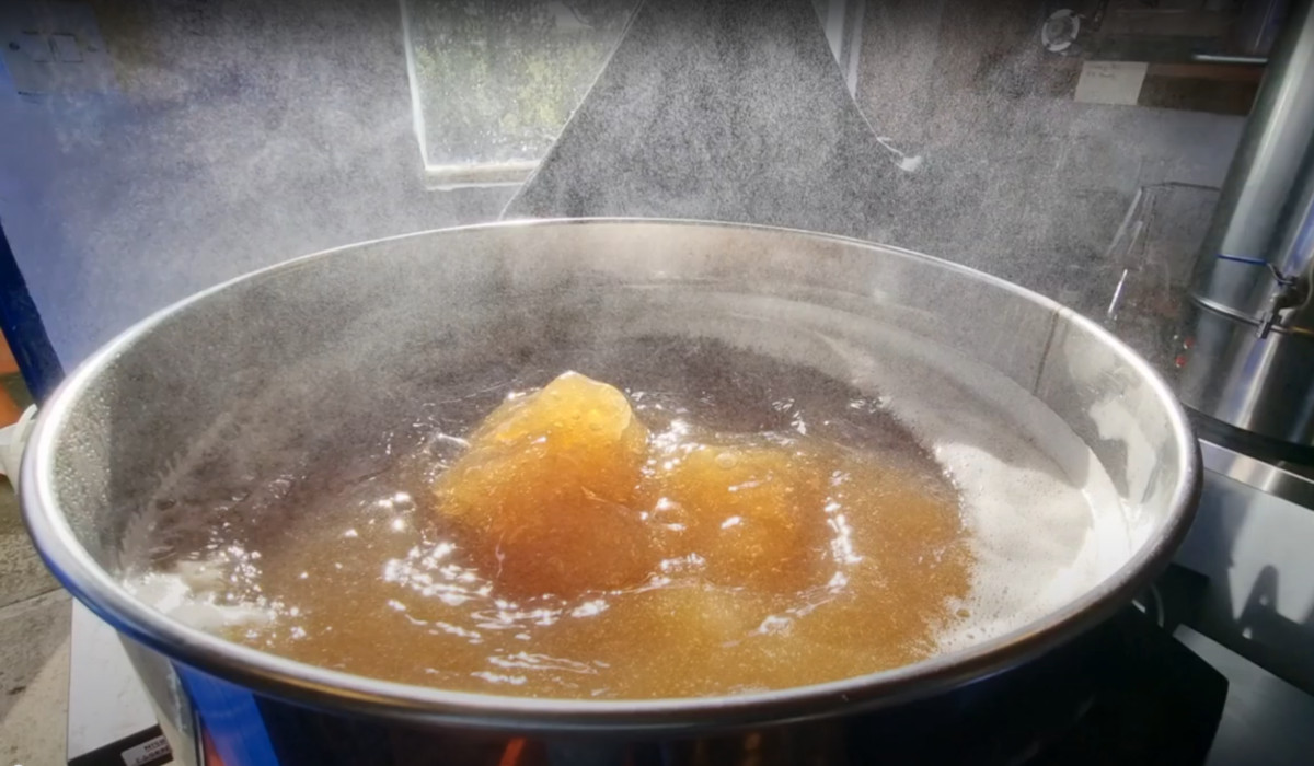 An open brew kettle with wort boiling vigorously. Steam rises from the brew kettle.