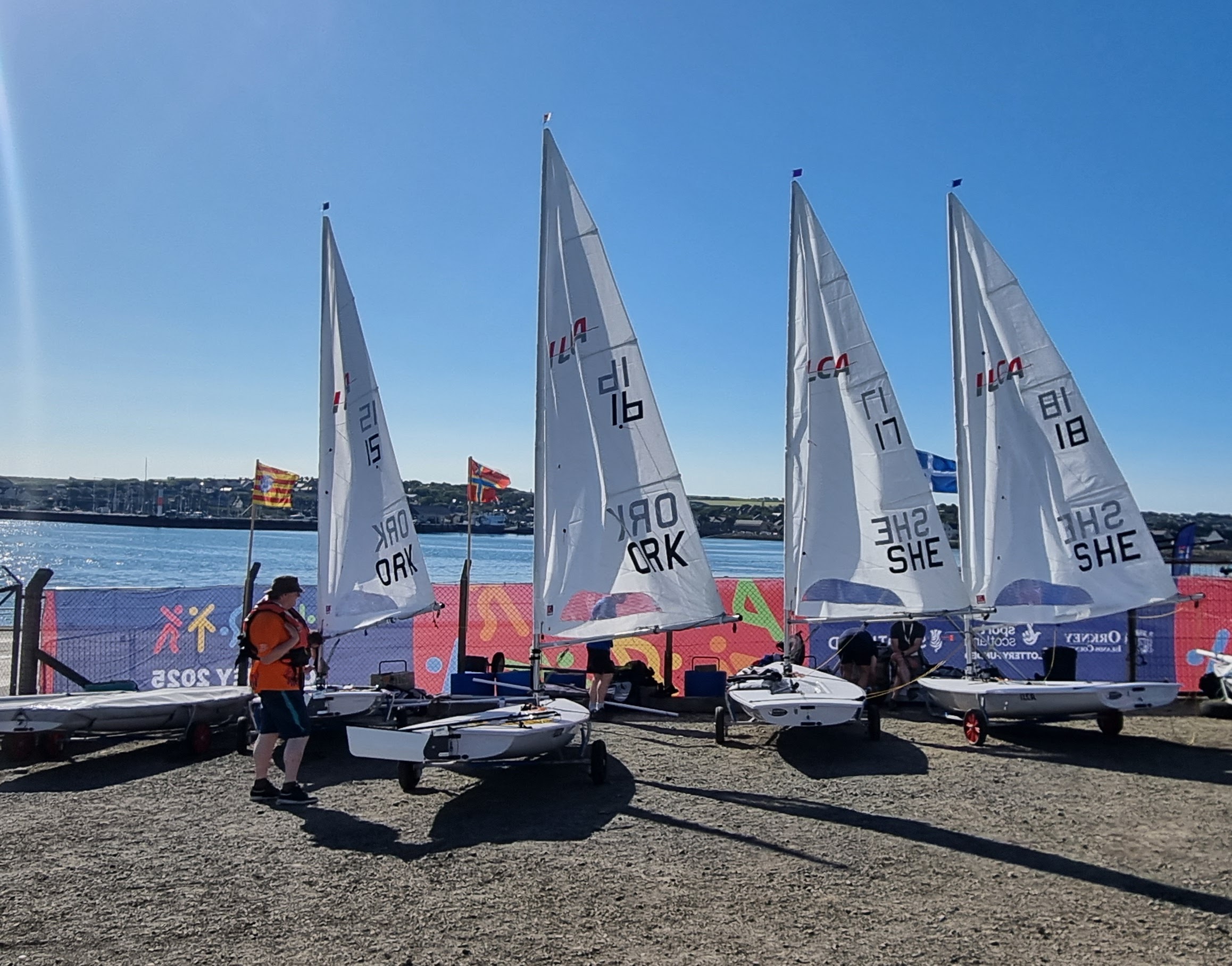 Two Orkney and two Shetland ILCA dinghies getting rigged to race in the Orkney Sailing Club compound at Hatston.
