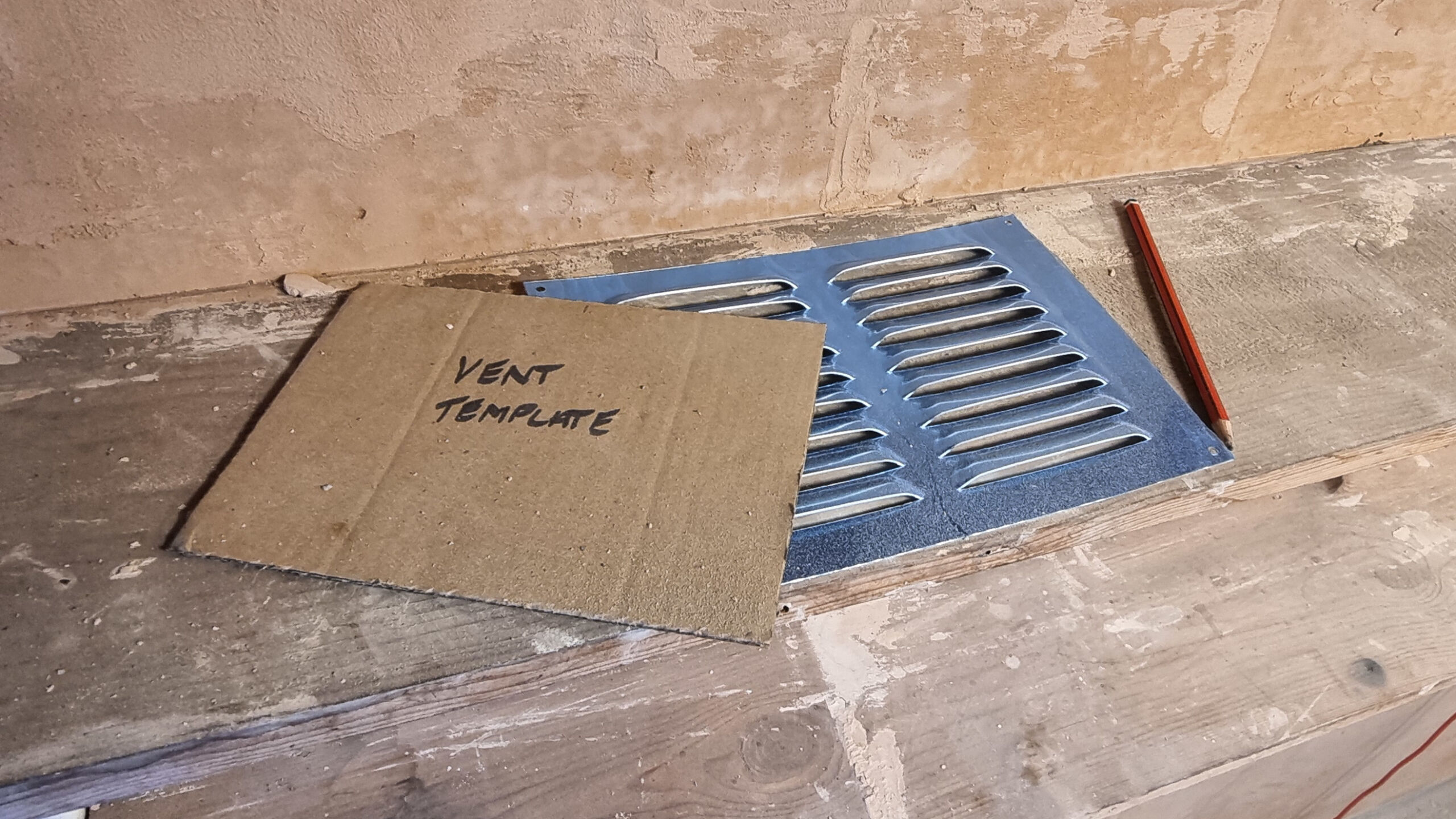 A cardboard ventilation template sits on a shelf on top of the metal grille to be installed.